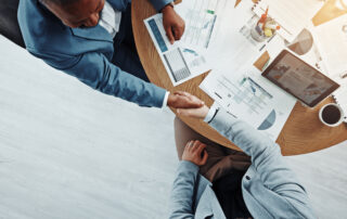 Two men in a business meeting shaking hands with papers on table.